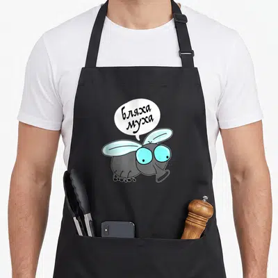 Tablier de cuisine noir avec mouche cartoon aux yeux bleus et bulle contenant du texte en alphabet cyrillique.