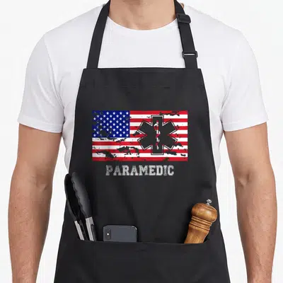 Tablier de cuisine noir avec drapeau ambulancier américain et le mot PARAMEDIC en blanc délavé au centre.