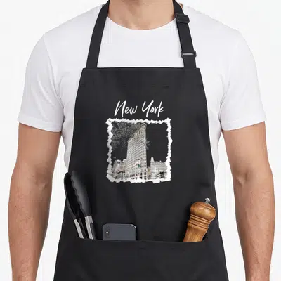 Tablier de cuisine noir avec une illustration du Flatiron Building encadrée d'un effet papier déchiré et le texte New York en haut.