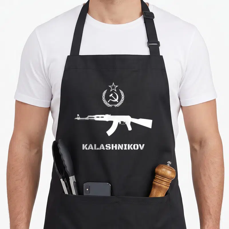 Tablier de cuisine noir avec silhouette fusil Kalashnikov, étoile, marteau faucille et inscription KALASHNIKOV en blanc.