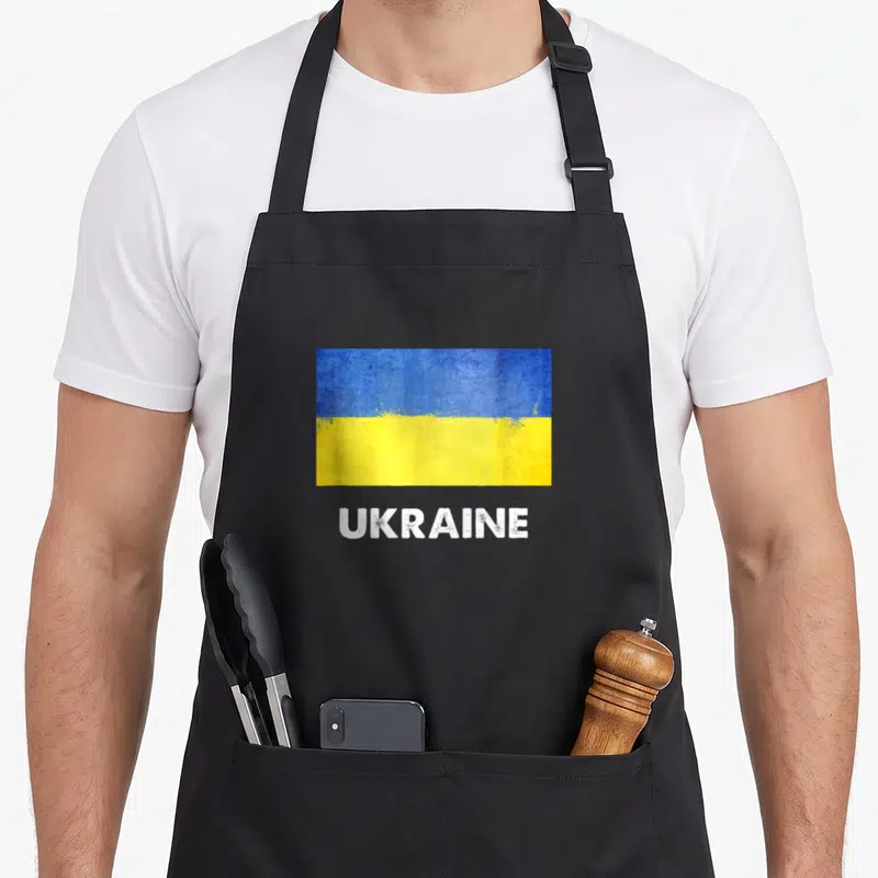 Tablier de cuisine noir avec drapeau Ukraine bleu et jaune texturé et inscription Ukraine en blanc sous le motif.