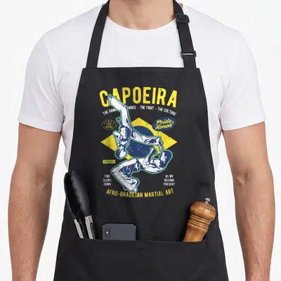 Tablier de cuisine noir avec illustration vintage de deux capoeiristes et le mot Capoeira en lettres jaunes.