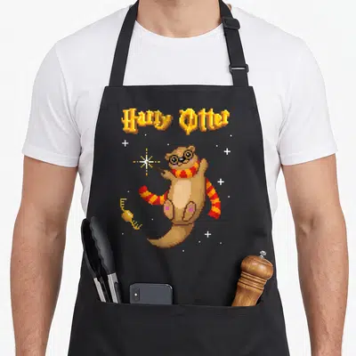 Tablier de cuisine noir avec illustration pixel art d'une loutre portant des lunettes et tenant une baguette magique sous le texte Harry Otter.