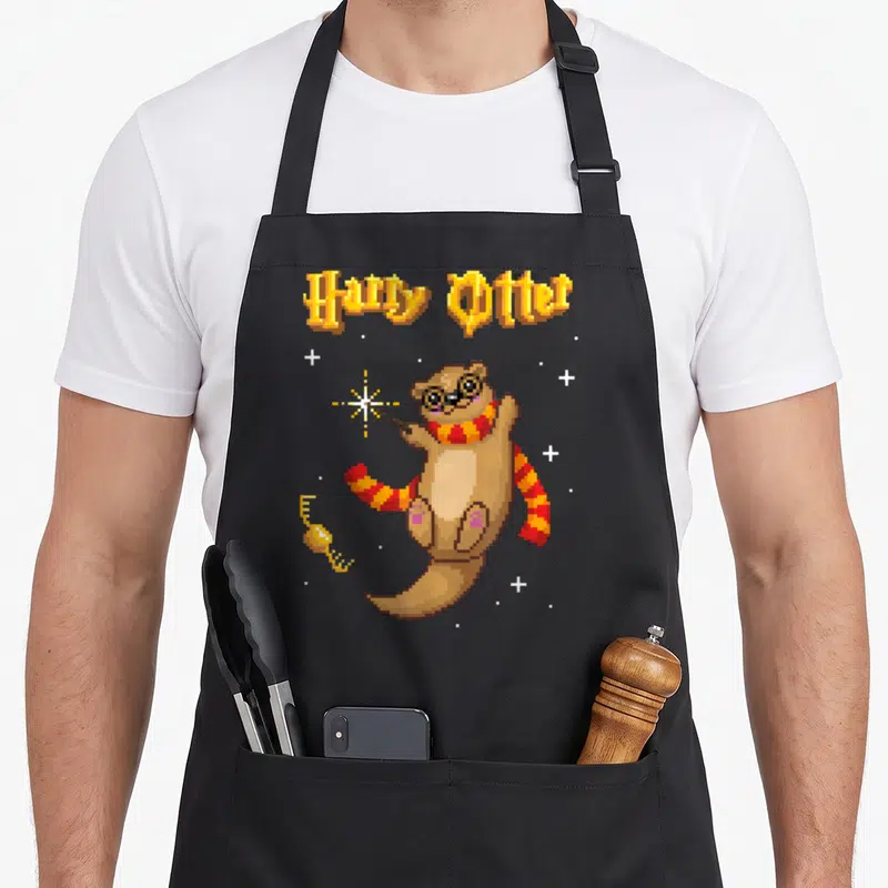 Tablier de cuisine noir avec illustration pixel art d'une loutre portant des lunettes et tenant une baguette magique sous le texte Harry Otter.