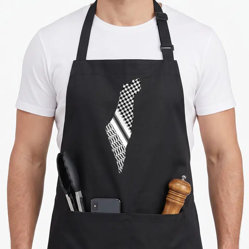 Tablier de cuisine noir avec une carte de Palestine remplie de motifs de keffiyeh et les mots Free Palestine Gaza Arabic imprimés.