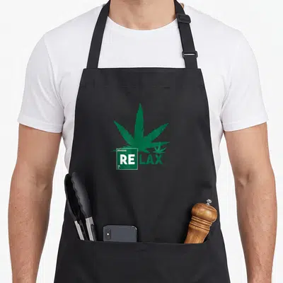 Tablier de cuisine noir avec une grande feuille de cannabis verte et l'inscription RE LAX en style tableau périodique.