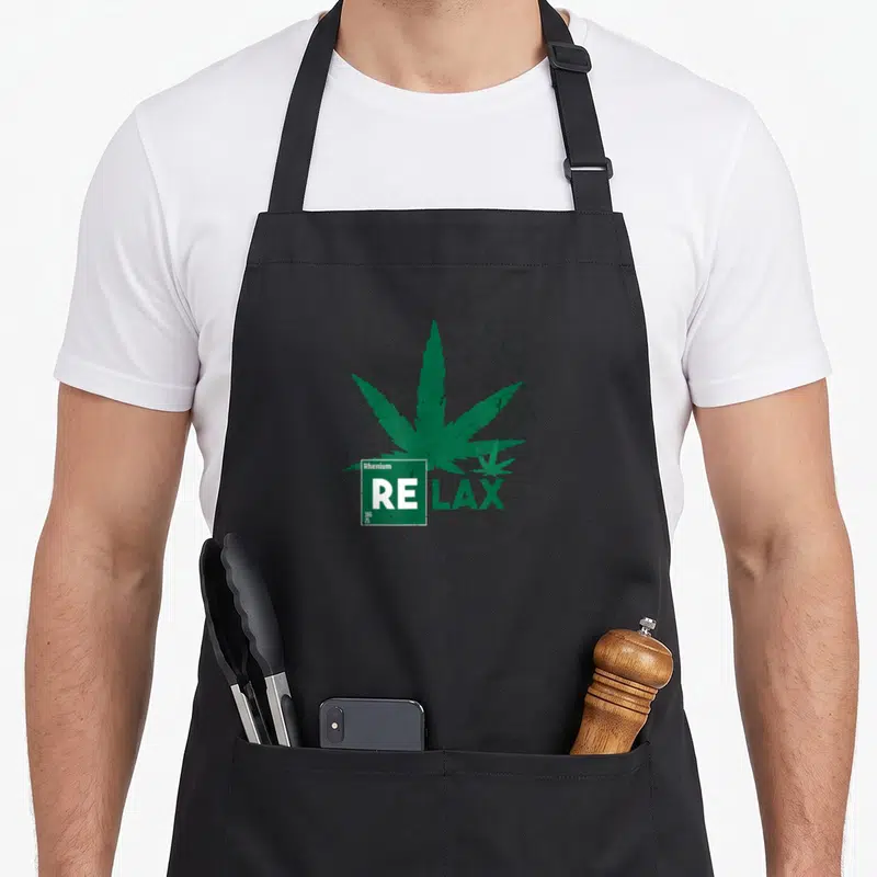 Tablier de cuisine noir avec une grande feuille de cannabis verte et l'inscription RE LAX en style tableau périodique.