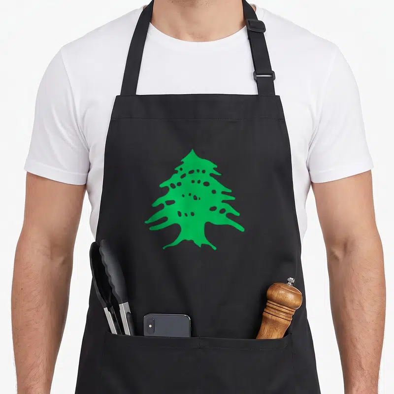 Tablier de cuisine noir avec un cèdre vert stylisé au centre, motif épuré sur fond sombre.