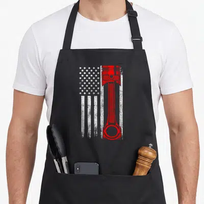 Tablier de cuisine noir avec illustration d'un piston rouge sur fond de drapeau américain en blanc et gris texturé.