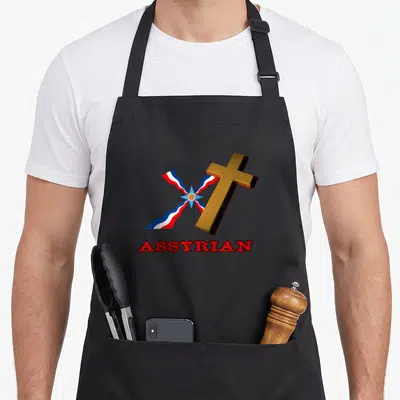 Tablier de cuisine noir avec une croix dorée, un drapeau rayé et le texte ASSYRIAN en lettres rouges.