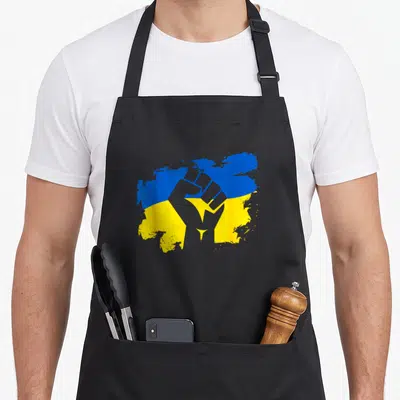Tablier de cuisine noir avec un poing levé gris superposé au drapeau bleu et jaune de l'Ukraine et un petit trident doré.