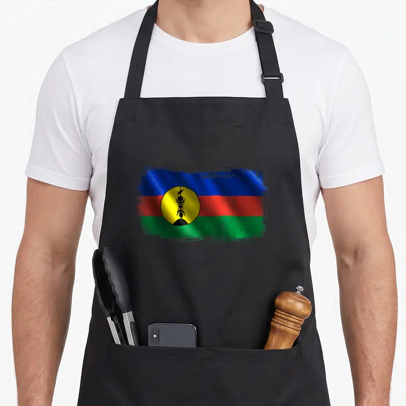 Tablier de cuisine noir avec drapeau de la Nouvelle-Calédonie aux couleurs vives et motif central circulaire jaune et noir.