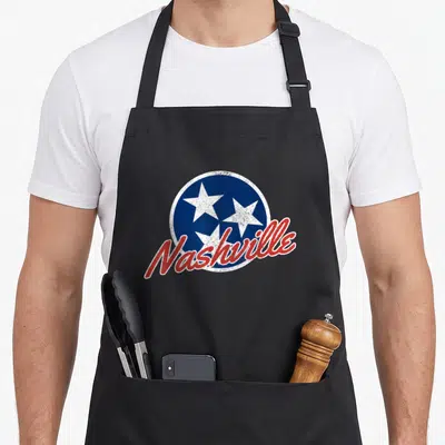Tablier de cuisine noir avec un logo circulaire bleu à trois étoiles et l'inscription Nashville en lettres rouges cursives.
