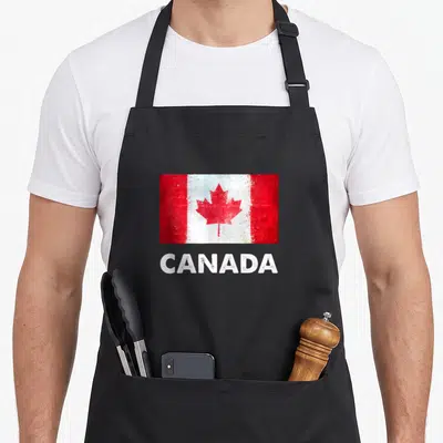 Tablier de cuisine noir avec drapeau canadien texturé et inscription CANADA en lettres blanches capitales.