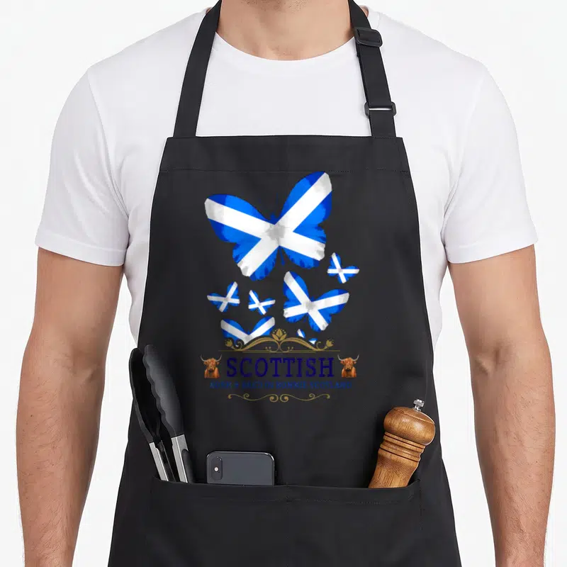 Tablier de cuisine noir avec des papillons au drapeau écossais, le mot Scottish et deux têtes de bœuf highland sur les côtés.