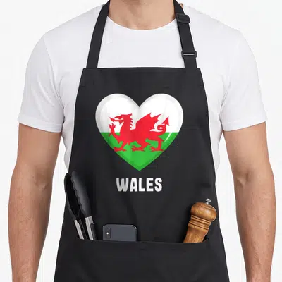 Tablier de cuisine noir avec un cœur affichant le drapeau gallois et le mot WALES en dessous.
