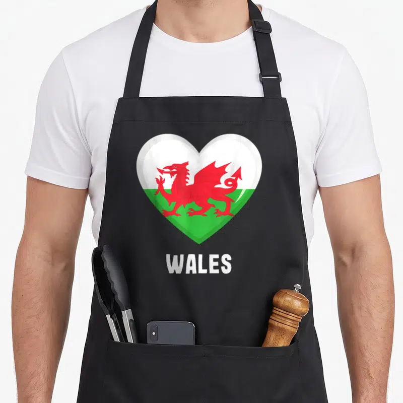 Tablier de cuisine noir avec un cœur affichant le drapeau gallois et le mot WALES en dessous.