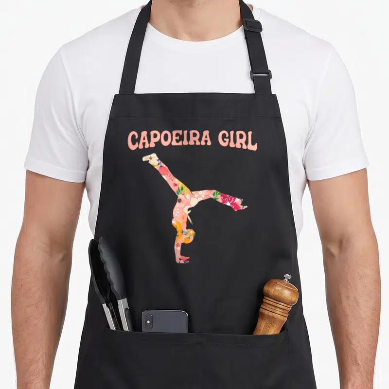 Tablier de cuisine noir avec une silhouette fleurie en acrobatie et l'inscription Capoiera Girl en rose
