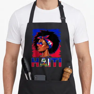 Tablier de cuisine noir avec illustration d'une femme haïtienne au chignon bandé rouge et bleu et le mot HAITI en lettres aux couleurs nationales.