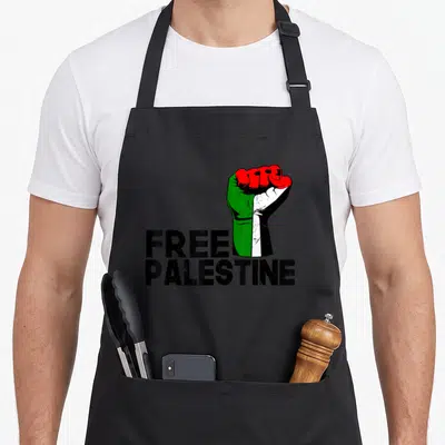 Tablier de cuisine noir avec un poing aux couleurs du drapeau palestinien et le texte Free Palestine imprimé en dessous.