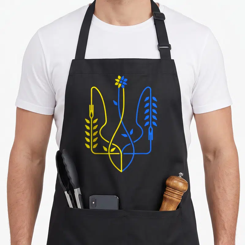 Tablier de cuisine noir avec un motif stylisé en lignes jaunes et bleues représentant des épis et une fleur centrale.