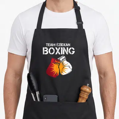 Tablier de cuisine noir avec l'inscription Team Êzidxan Boxing sur deux gants de boxe rouge et blanc à motif solaire.