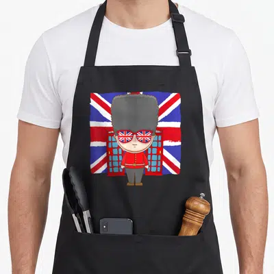 Tablier de cuisine noir avec illustration d'un soldat royal aux lunettes drapeau Union Jack devant des bornes téléphoniques rouges.