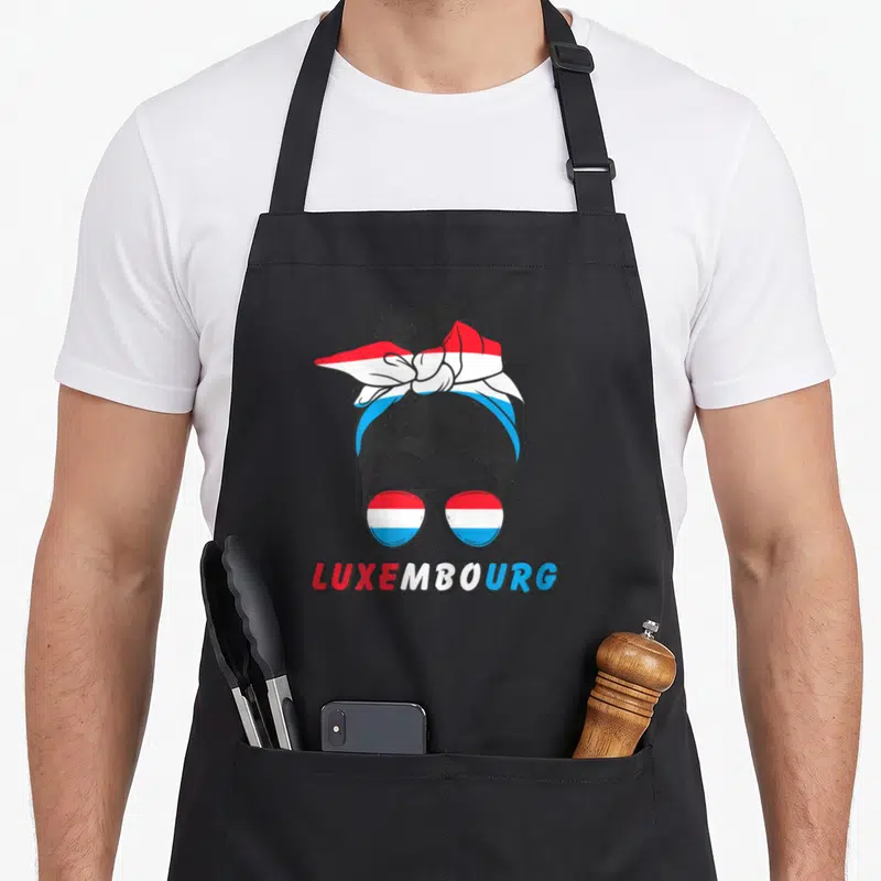 Tablier de cuisine noir avec illustration de chignon, foulard tricolore et lunettes portant l'inscription LuxemboURG.