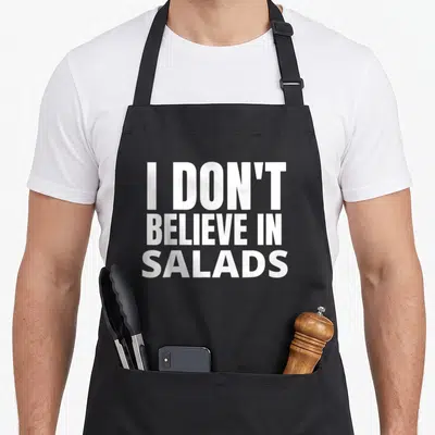 Tablier de cuisine noir avec l'inscription blanche en majuscules I DON'T BELIEVE IN SALADS au centre.