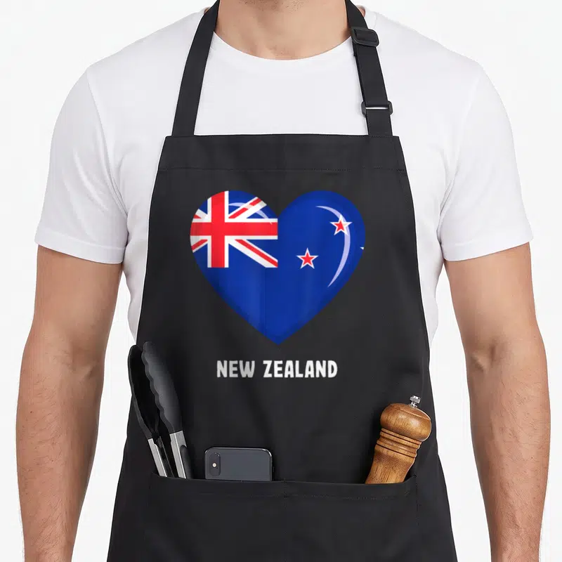 Tablier de cuisine noir avec un grand cœur affichant le drapeau de la Nouvelle-Zélande et l'inscription NEW ZEALAND en blanc.