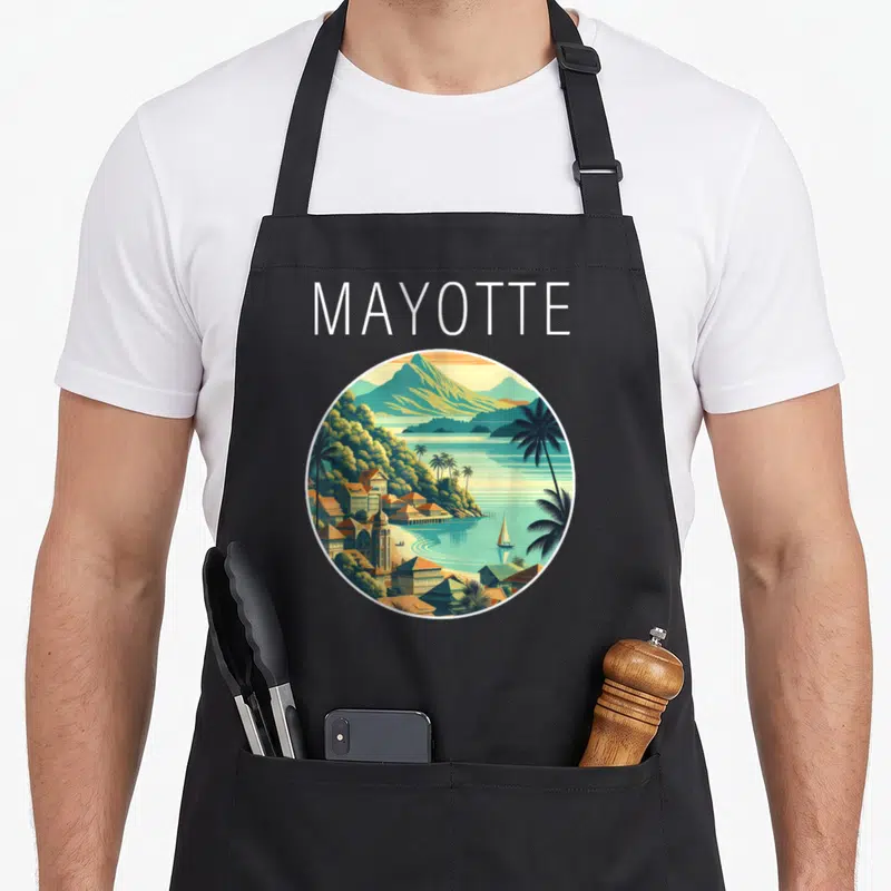 Tablier de cuisine noir avec illustration circulaire d'un paysage de Mayotte aux couleurs chaudes et palmiers.