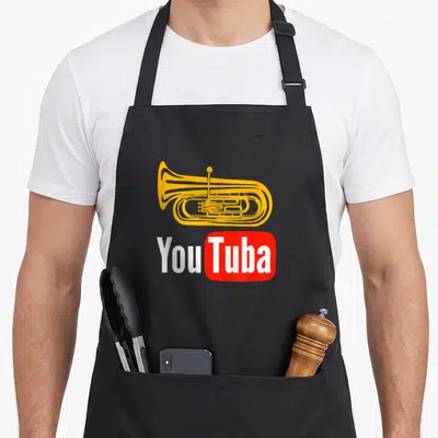 Tablier de cuisine noir avec illustration d'un tuba jaune et l'inscription YouTuba en blanc sur fond rouge.
