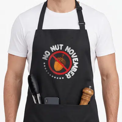 Tablier de cuisine noir avec un acorn barré en rouge et l'inscription No Nut November challenge en lettres blanches.