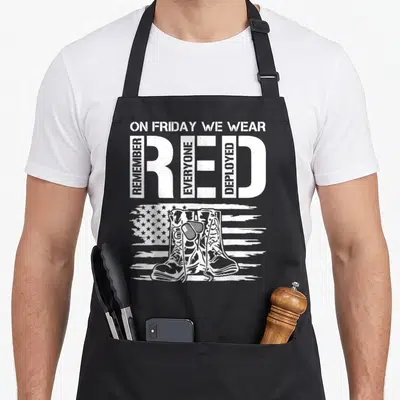 Tablier de cuisine noir avec texte blanc On Friday Nous Portons Rouge Red et illustration de bottes militaires sur fond de drapeau américain stylisé.
