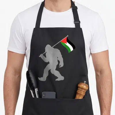 Tablier de cuisine noir avec silhouette de singe portant le drapeau Palestine aux couleurs vives.