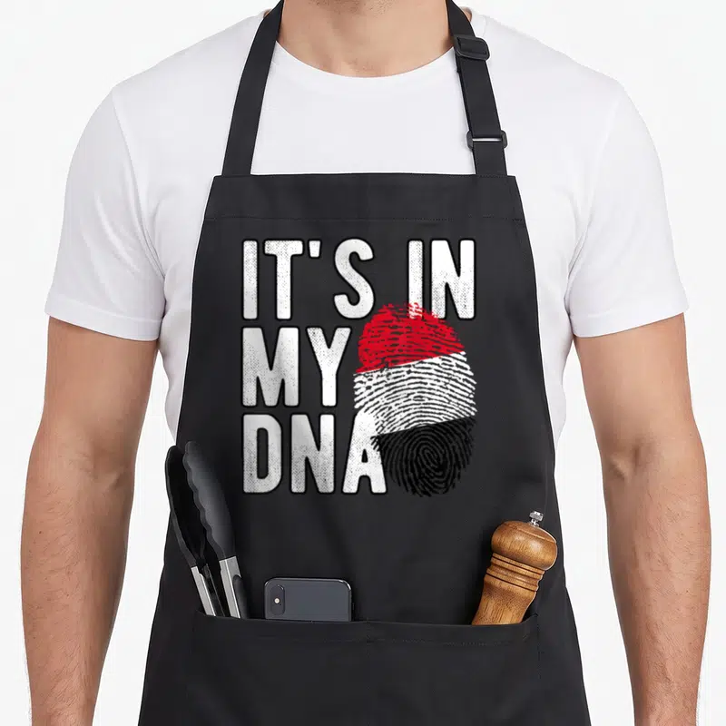 Tablier de cuisine noir avec l'inscription It's in my DNA et une empreinte au drapeau du Yémen