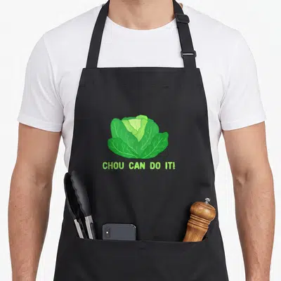 Tablier de cuisine noir avec illustration d'un chou vert et le texte CHOU CAN DO IT. en lettres capitales vertes claires.