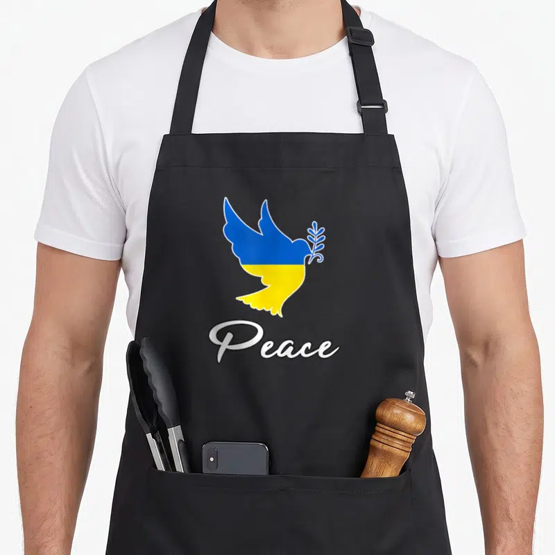 Tablier de cuisine noir avec colombe bleue et jaune tenant une branche et le mot Peace écrit en blanc.