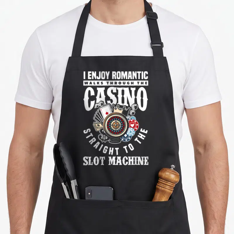 Tablier de cuisine noir avec illustration de roulette, cartes à jouer, pions et texte blanc sur fond gris.