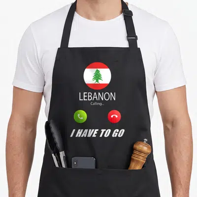 Tablier de cuisine noir avec un drapeau Liban en cercle, les mots Lebanon Calling et I Have To Go sous des icônes téléphoniques.