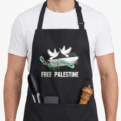 Tablier de cuisine noir avec drapeau palestinien, colombes blanches et chaîne verte brisée sous l'inscription Free Palestine.