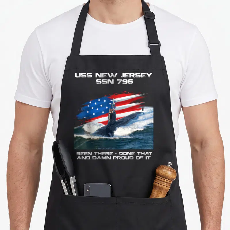 Tablier de cuisine noir avec illustration sous-marin USS New Jersey SSN 796 et drapeau américain en arrière-plan dynamique.