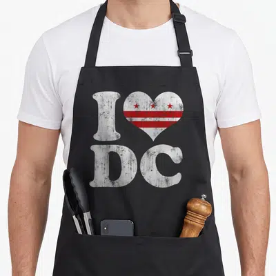 Tablier de cuisine noir avec un cœur stylisé contenant les étoiles rouges et bandes du drapeau DC sous la lettre I.