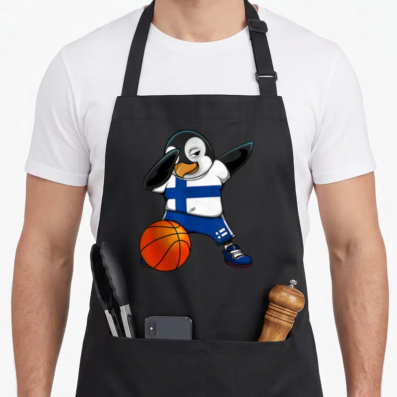 Tablier de cuisine noir avec un pingouin effectuant une pose dab en tenant un ballon de basket orange, vêtu d'un maillot finlandais.