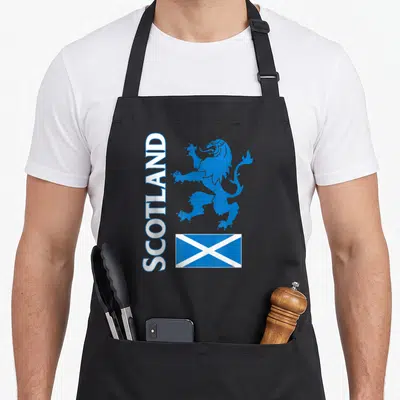 Tablier de cuisine noir avec inscription SCOTLAND, lion rampant bleu et drapeau écossais en bas à droite.