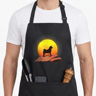 Tablier de cuisine noir avec silhouette d'Akita Américain devant un soleil orange et jaune.
