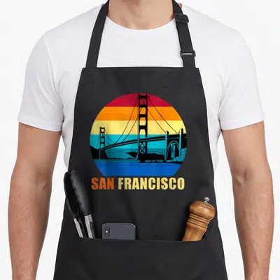 Tablier de cuisine noir avec un motif circulaire coloré du Golden Gate Bridge et l'inscription San Francisco en bas.