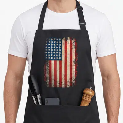 Tablier de cuisine noir avec un drapeau américain aux couleurs vives et effet vieilli sur le devant.