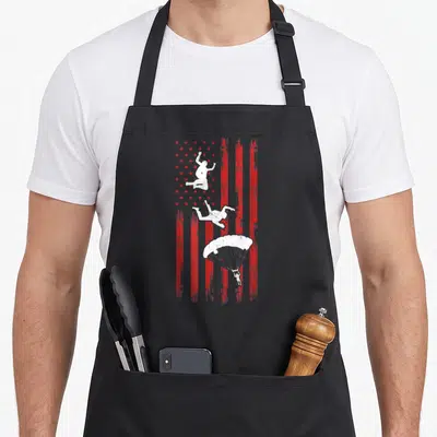Tablier de cuisine noir avec un drapeau américain rouge et blanc et trois silhouettes de parachutistes en chute libre.