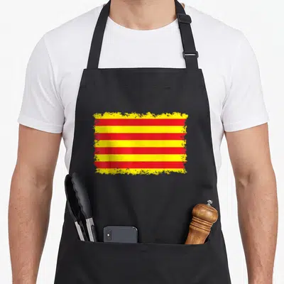 Tablier de cuisine noir avec le drapeau catalan aux bandes rouges et jaunes aux bords estompés.